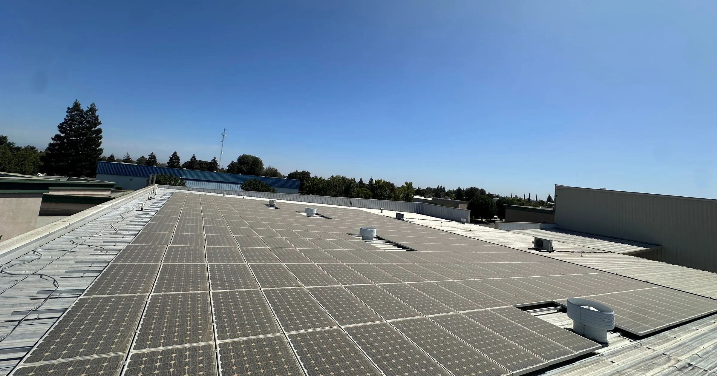 Rows of rooftop solar panels coated in a gray layer of dust under a clear blue sky